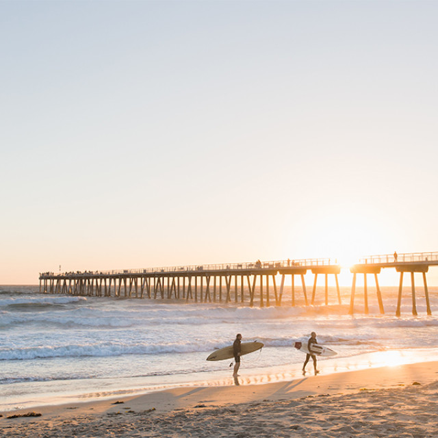 Surfers walk near Hermosa Beach Pier in Los Angeles, California